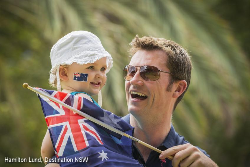 A father holding a young child with an Australian flag. Photo: Hamilton Lund, Destination NSW.